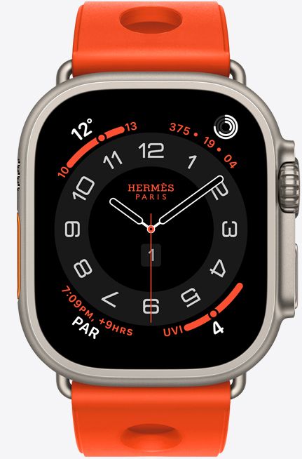 Apple Watch Hermès Ultra 3, Circulaire analog watch face, (hour, minute and second hands, complications: Weather, activity rings, Paris time and UV Index), titanium case, natural colour, right side exterior, Digital Crown, raised side button, paired with Scub'H Diving band, orange néon colour (bright orange), molded rubber material, circular cutouts centred
