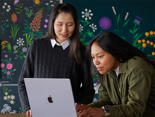 Dos personas del equipo de Marketing de Apple trabajan juntos en una MacBook delante de carteles diseñados por su equipo.