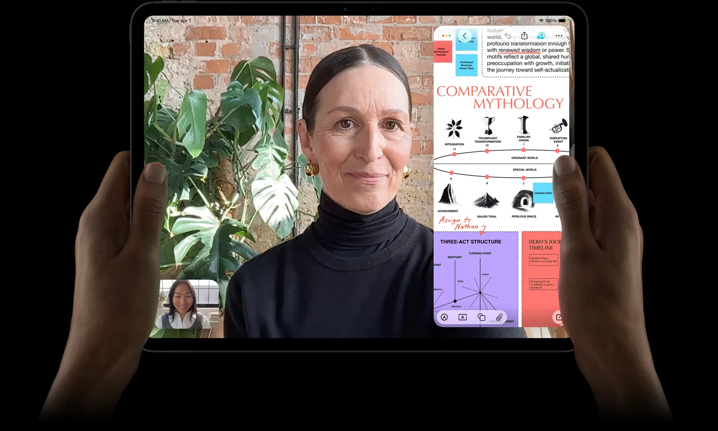 iPad Pro, front exterior, space black color, left and right hands holding in landscape orientation, rounded corners, black display bezel, display showing a FaceTime conversation being live translated, and an educational app showing a presentation of 'Comparative Mythology' with text, diagrams, and handwritten notes