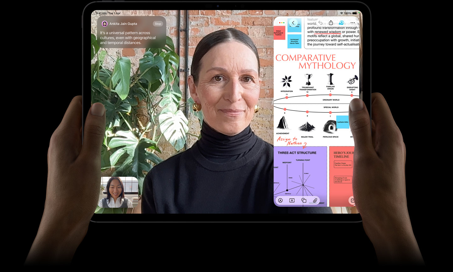 iPad Pro, front exterior, space black colour, left and right hands holding in landscape orientation, rounded corners, black display bezel, display showing a FaceTime conversation being live translated and an educational app showing a presentation of 'Comparative Mythology' with text, diagrams and handwritten notes