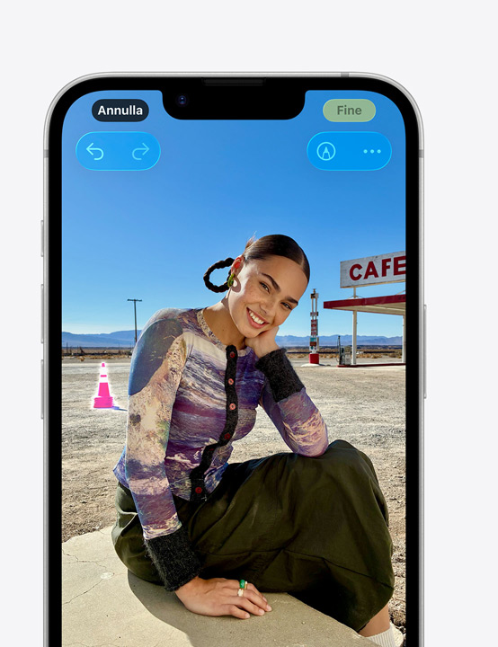 iPhone che mostra la foto di una persona sorridente, e l’uso dello strumento Ripulisci per rimuovere un cono segnaletico sullo sfondo