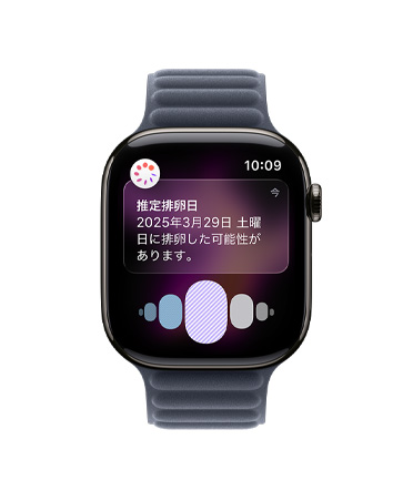 スレートチタニウムケースのApple Watch Series 11。ヘルスケアアプリの周期記録から推定される排卵日の通知が表示されている。Digital Crownが見えていて、ネイビーのマグネティックリンクバンドが取りつけられている