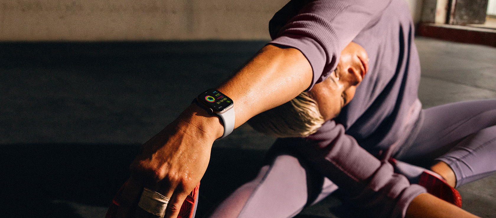 ผู้หญิงนั่งบนพื้นอยู่ในท่าเหยียดแขนพร้อมโน้มตัวไปแตะขากำลังสวม Apple Watch Series 10