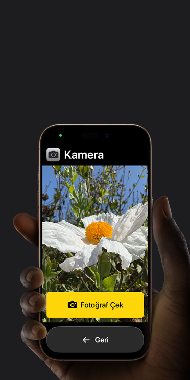 Kadrajında beyaz çiçek bulunan Kamera uygulamasının basitleştirilmiş arayüzünü, “Fotoğraf Çek” düğmesini ve altındaki “Geri” düğmesini gösteren iPhone 16 Pro ekranı