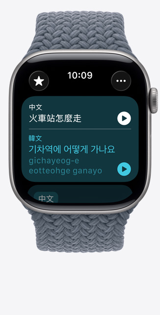 Apple Watch Series 11，展示太空灰色鋁金屬錶殼，搭配錨藍色編織單圈錶環，螢幕上的「翻譯」app 顯示要怎麼去火車站的韓文翻譯和發音