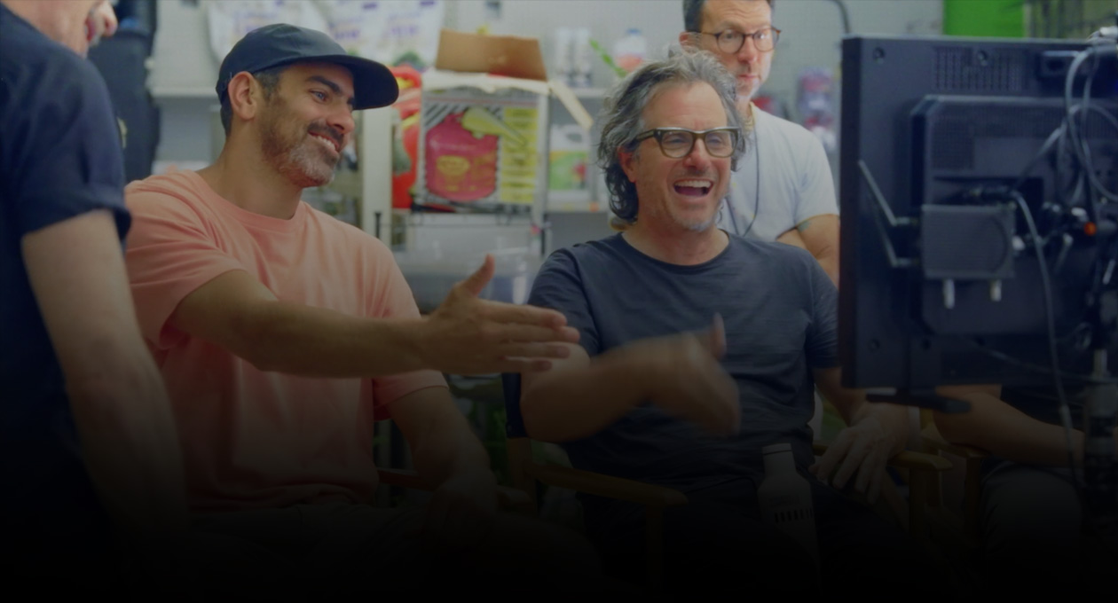 Imagen de dos cineastas sentados que miran y hacen gestos hacia la pantalla de proyección.