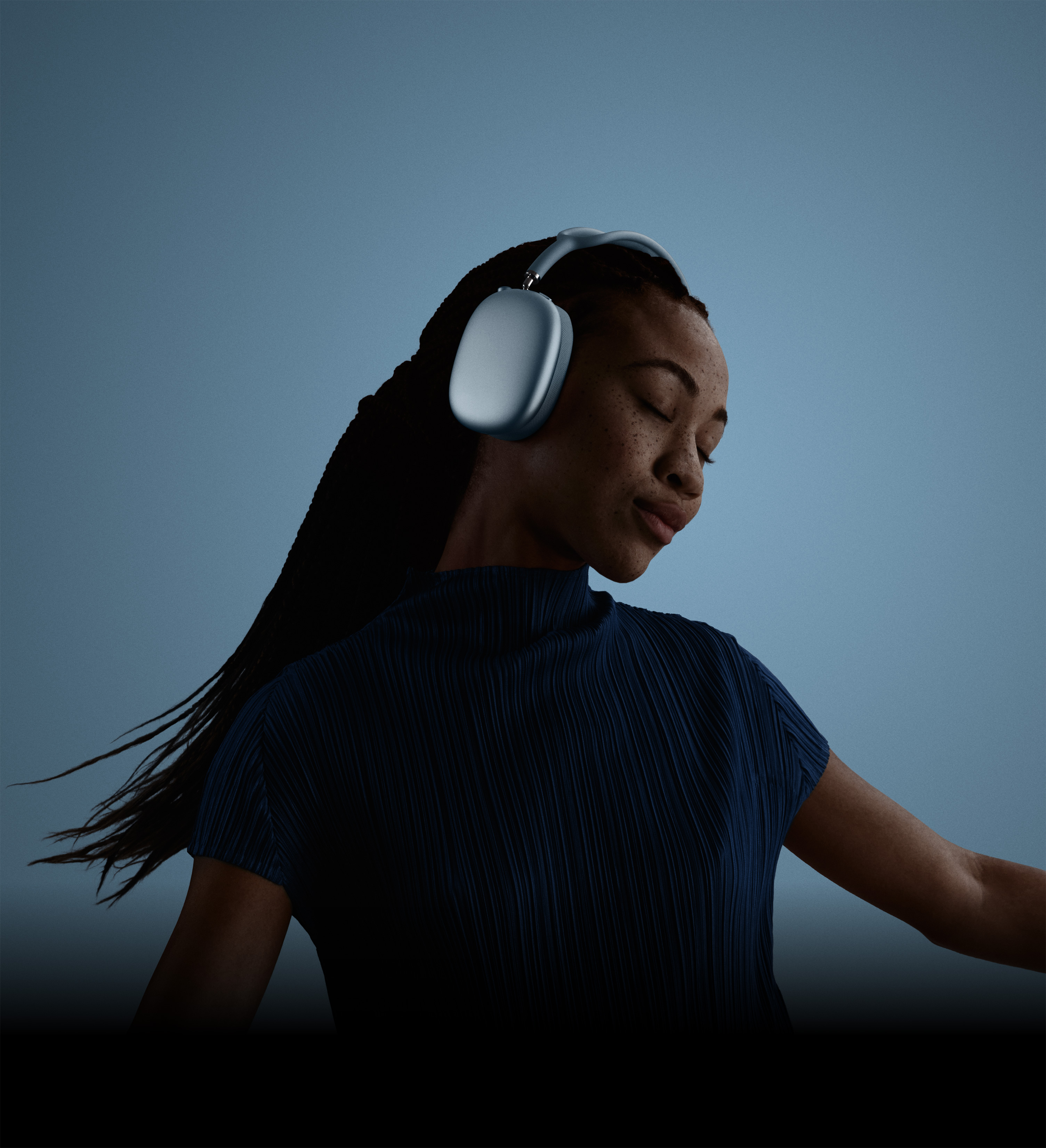 A person with eyes closed and head tilted, side profile, wearing AirPods Max 2 headphones in blue colour.