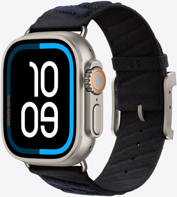 Apple Watch Hermès Ultra 3, titanium case, natural colour, edge-to-edge display, rounded corners, right side exterior, Digital Crown, microphone, raised side button, digital watch face (10 09 time digits), paired with En Mer strap, noir/bleu nuit colour (black with dark blue diagonal textured stripes), knit polyamide yarn material, adjustment holes centred, natural colour titanium buckle and hardware