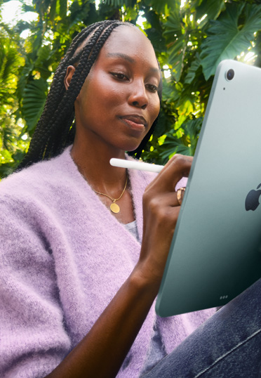 Seorang mahasiswi sedang duduk di luar ruangan. Dia memegang iPad dan Apple Pencil Pro.