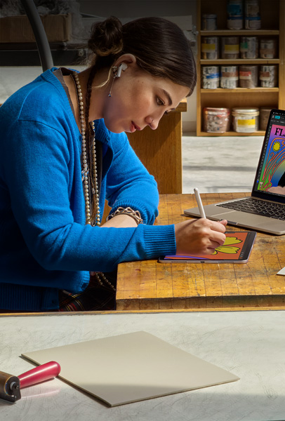 寮の部屋で、シルバーのMacBookでコンテンツを見る2人の学生。1人はベッドに座り、もう1人はデバイスを持って床に座っている