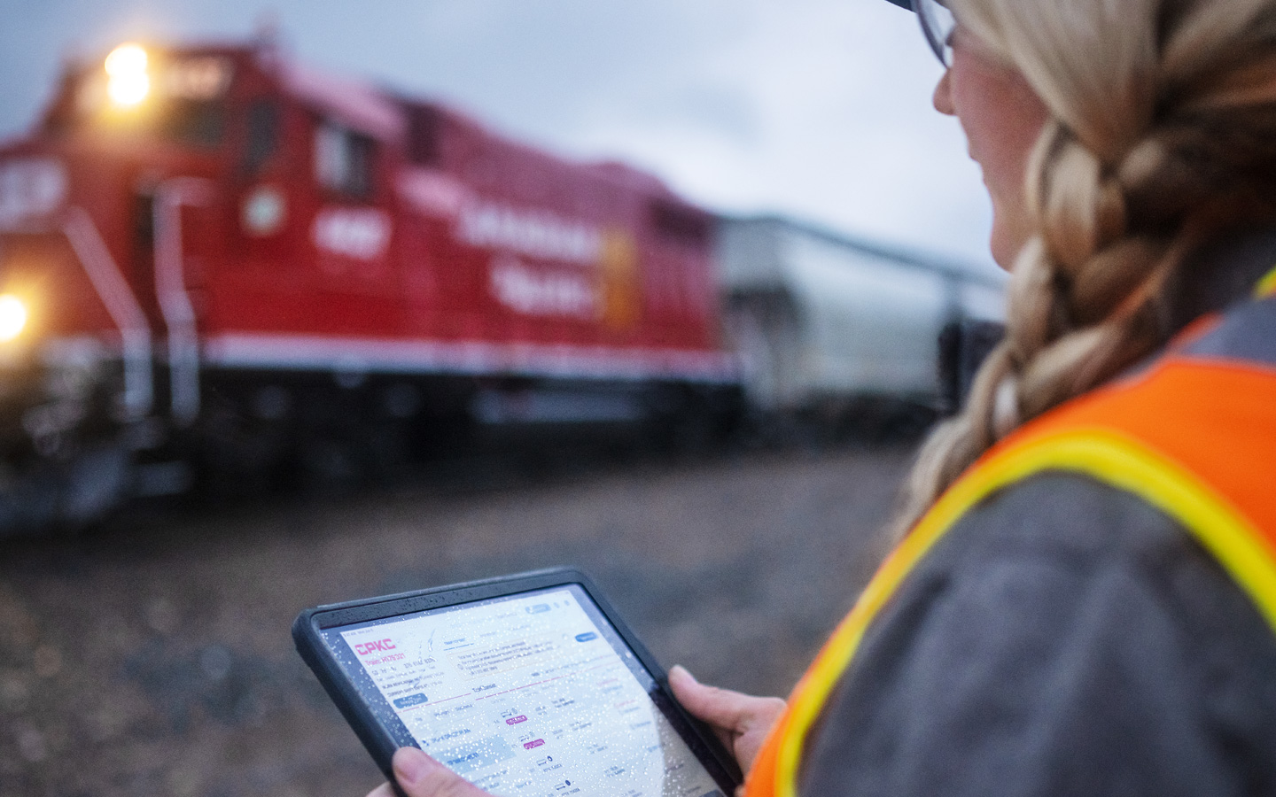 操車場に立つ鉄道員が、iPadで列車の時刻表を確認している