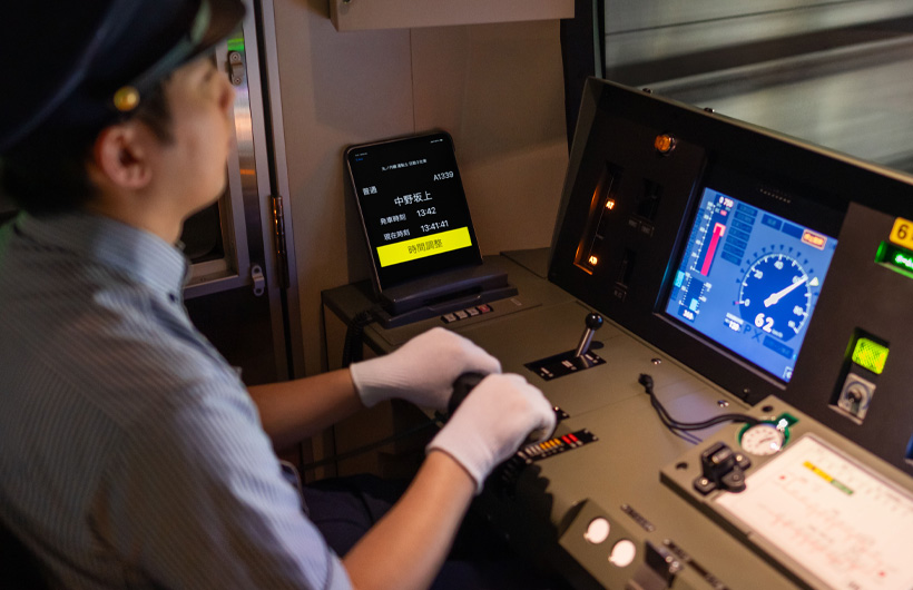 Un iPad affichant les stations et les horaires est posé près de la console de contrôle, où travaille un conducteur de train.