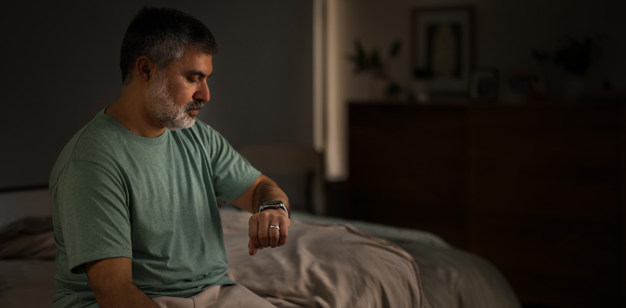 Un homme, assis sur son lit, consulte son Apple Watch.