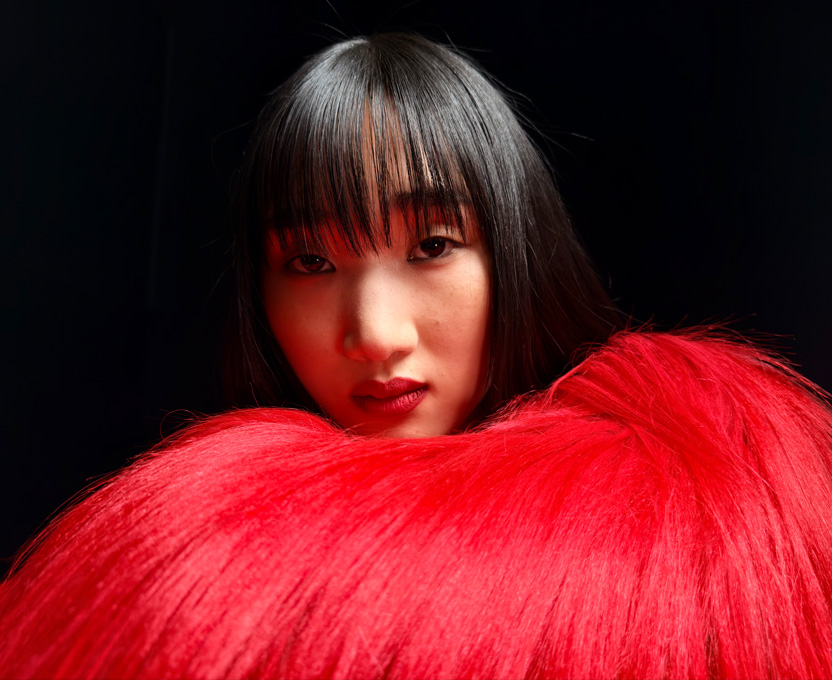 一名身穿亮紅色羽毛上衣的女子特寫，展示 iPhone 17 Pro 的超高解析度攝影功能
