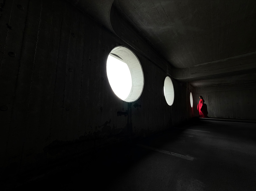 A woman wearing a long red dress stands in an empty room being photographed. The Photo app toggles through the following focal lengths to demonstrate the capabilities of the pro camera system: 200 mm, 100 mm, 48 mm, 35 mm, 28 mm, 13 mm and macro