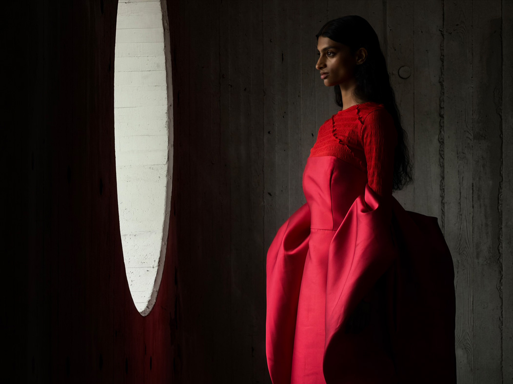 A woman wearing a long red dress stands in an empty room being photographed. The Photo app toggles through the following focal lengths to demonstrate the capabilities of the pro camera system: 200 mm, 100 mm, 48 mm, 35 mm, 28 mm, 13 mm and macro