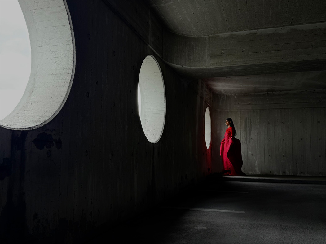 A woman wearing a long red dress stands in an empty room being photographed. The Photo app toggles through the following focal lengths to demonstrate the capabilities of the pro camera system: 200 mm, 100 mm, 48 mm, 35 mm, 28 mm, 13 mm and macro