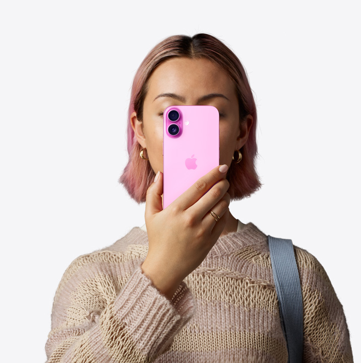 Persona sujetando un iPhone 16 en color rosa delante de su cara que muestra la parte trasera, sistema de cámara dual en la esquina superior izquierda.