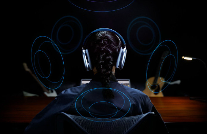Une personne de dos, portant des AirPods Max d’Apple, avec des images circulaires autour de sa tête représentant l’audio spatial