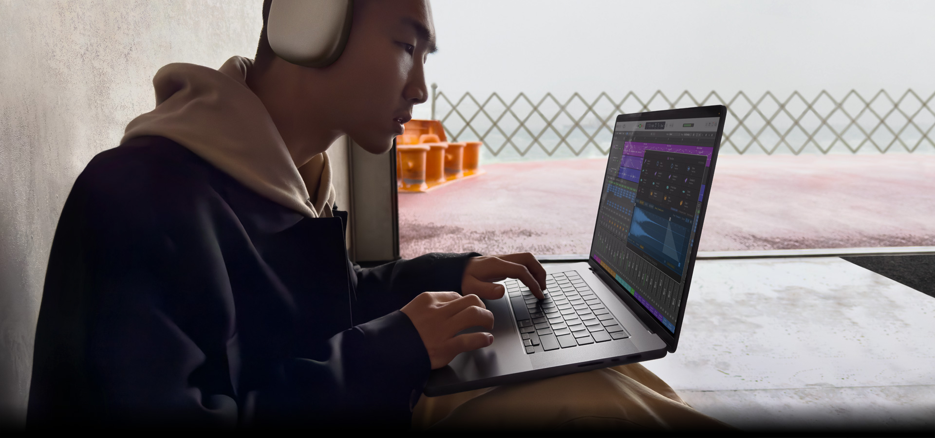 Une personne de profil, portant des AirPods Max et utilisant Logic Pro sur un MacBook Pro 16 pouces, l’écran affiche l’espace de travail Logic Pro