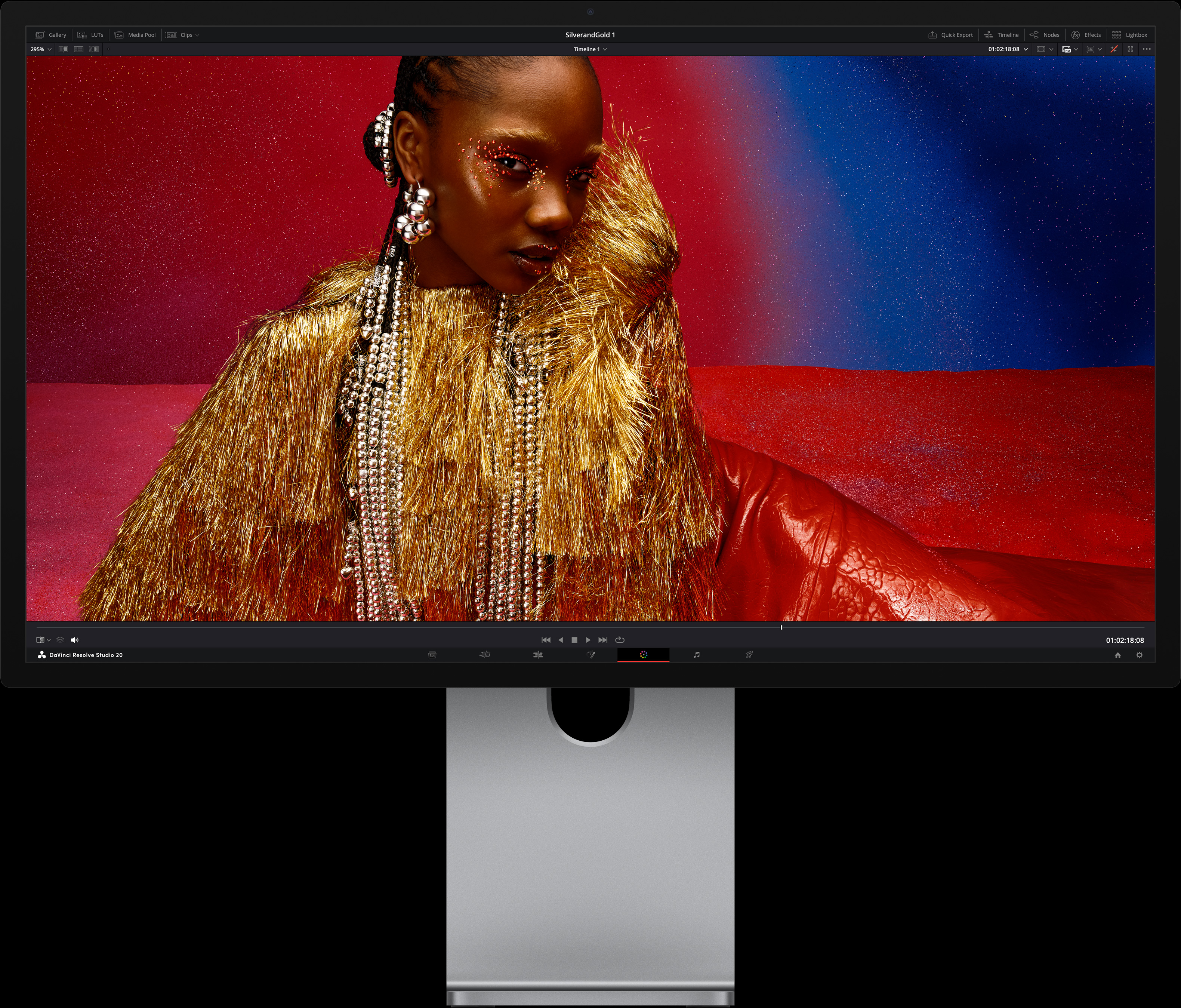 Une personne portant une robe rouge vif et des accessoires métalliques surdimensionnés est assise devant un arrière-plan affichant un dégradé de bleu et rouge, illustrant la qualité d’image du Studio Display XDR