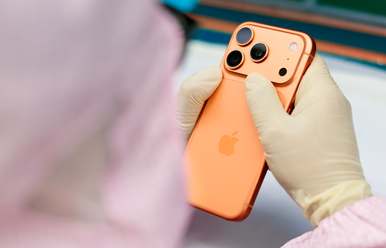 フルカバーの作業服を着た1人の従業員がワークステーションでiPhoneを検査している