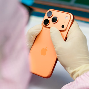 フルカバーの作業服を着た1人の従業員がワークステーションでiPhoneを検査している