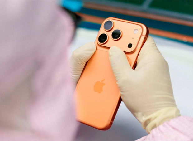 フルカバーの作業服を着た1人の従業員がワークステーションでiPhoneを検査している